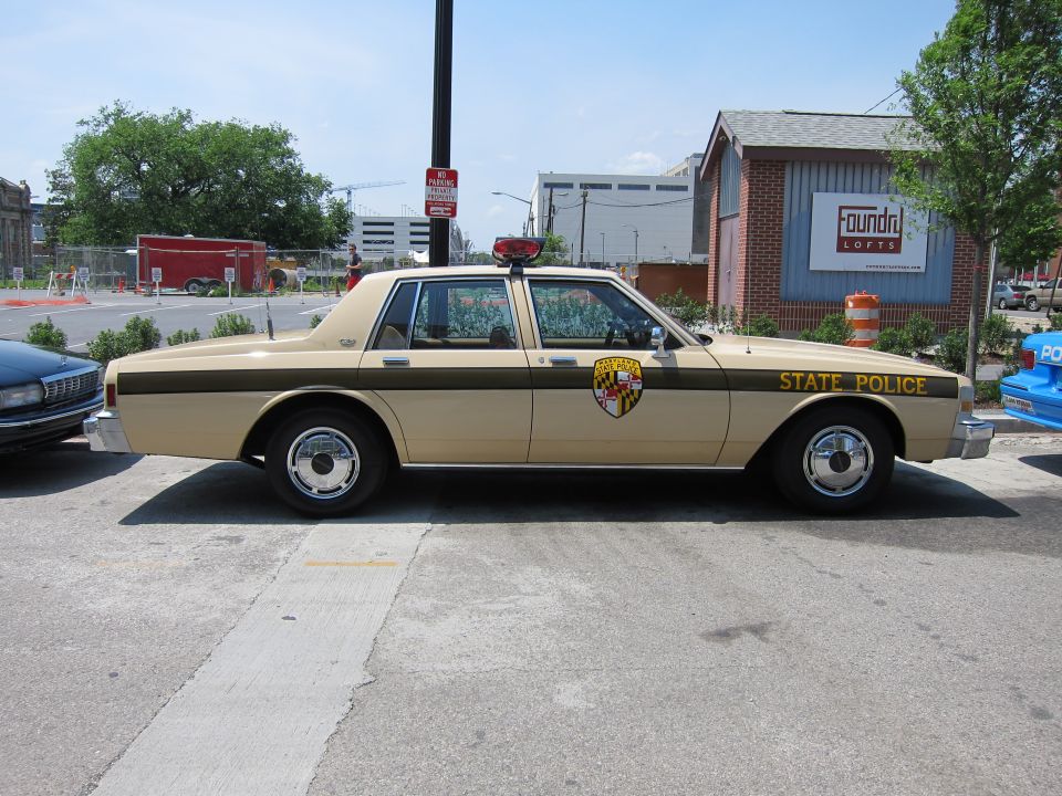 Tan and brown Maryland State Police sedan parked at a curb in profile