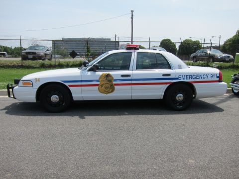 1991 Ford LTD Crown Victoria - Side view of a white Ford Crown Victoria unit 34 lettered Emergency 911 with a gold badge decal.