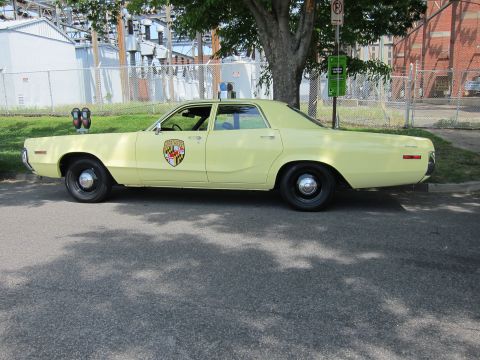 1991 Ford LTD Crown Victoria - Side profile of a pale yellow vintage police sedan bearing a Maryland shield and roof lights.