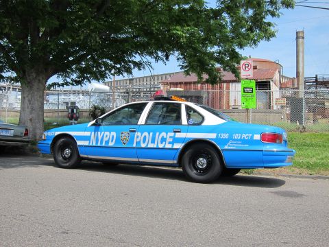 1991 Ford LTD Crown Victoria - blue and white NYPD POLICE sedan numbered 1350 103 PCT is shown in rear three-quarter view parked under a tree by a fence.