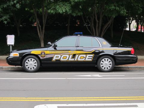 1991 Ford LTD Crown Victoria - black Ford Crown Victoria Police Interceptor with yellow POLICE graphics and a blue roof bar sits in profile along a curbed street.