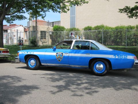 1991 Ford LTD Crown Victoria - blue and white two-door vintage police car marked POLICE 1162 with a roof beacon sits in profile beside a chain-link fence.