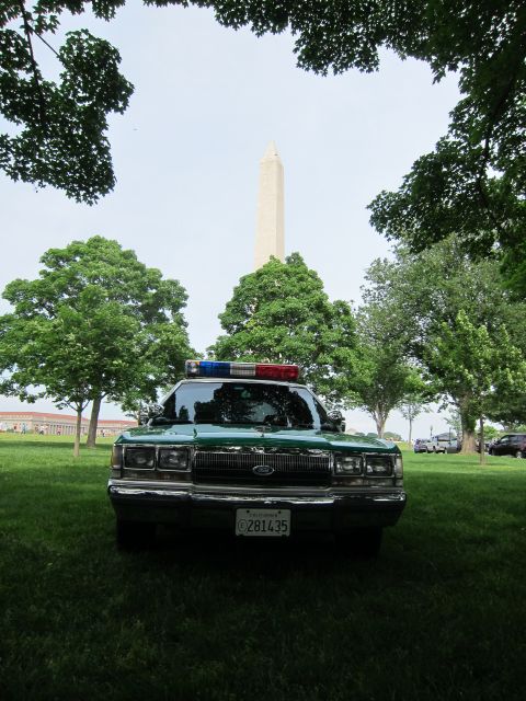 1991 Ford LTD Crown Victoria - green and white Ford full-size sedan with a roof light bar is parked on grass with the Washington Monument rising behind trees.