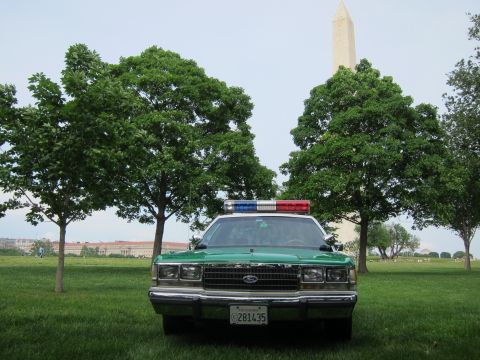 1991 Ford LTD Crown Victoria - green and white Ford full-size sedan with a roof light bar is parked among young trees with the Washington Monument rising behind.