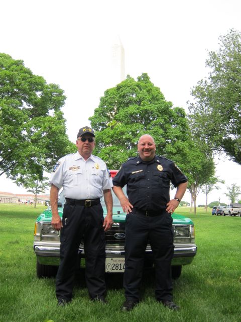 1991 Ford LTD Crown Victoria - Two men in dark uniforms stand in front of a green and white Ford sedan on a lawn with the Washington Monument behind trees.