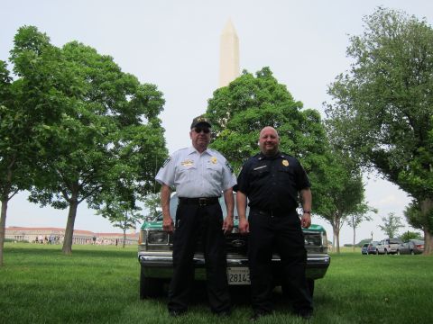 1991 Ford LTD Crown Victoria - Two men in dark uniforms pose in front of a green and white Ford sedan on grass with the Washington Monument and trees behind them.