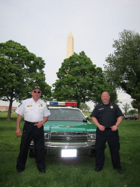 1991 Ford LTD Crown Victoria - Two uniformed officers pose in front of a green-and-white Ford police cruiser with the Washington Monument rising in the background.