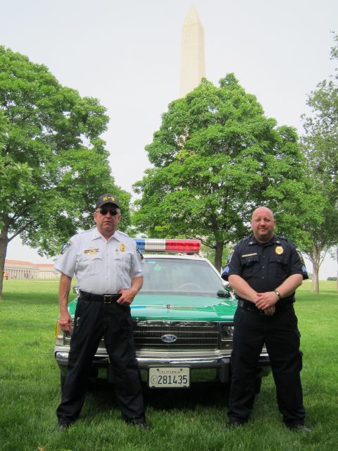 1991 Ford LTD Crown Victoria - Two uniformed officers pose beside a green-and-white police sedan on grass with the Washington Monument visible through the trees.