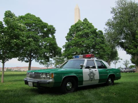 1991 Ford LTD Crown Victoria - green-and-white police sedan with a star door emblem and roof lightbar is parked on a lawn near the Washington Monument.