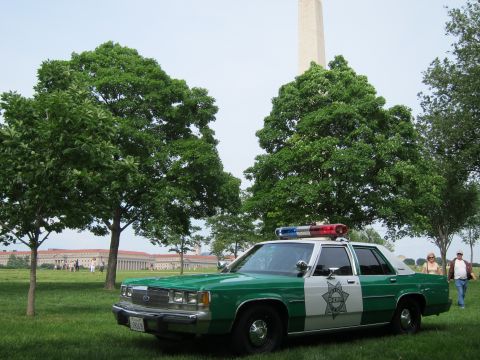 1991 Ford LTD Crown Victoria - green-and-white police sedan bearing a star emblem on the door is parked on a lawn with the Washington Monument in the distance.