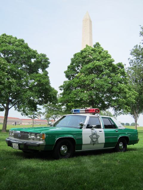 1991 Ford LTD Crown Victoria - green-and-white police cruiser with roof lightbar and door star emblem rests on grass in front of the Washington Monument.