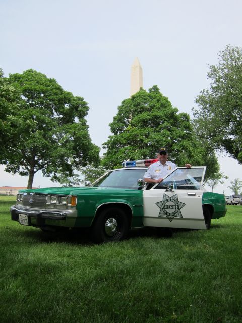 1991 Ford LTD Crown Victoria - officer stands at the open door of a green-and-white Sheriff cruiser parked on a lawn near the Washington Monument.