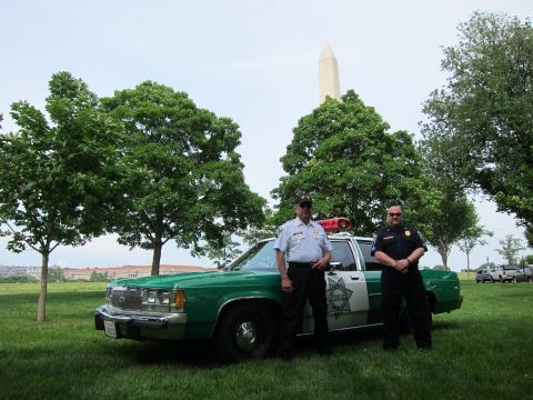 1991 Ford LTD Crown Victoria - Two officers stand beside a green-and-white police sedan on grass with the Washington Monument visible through the trees.