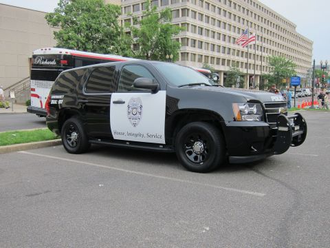 1991 Ford LTD Crown Victoria - black-and-white Chevrolet Tahoe police SUV marked 'Honor, Integrity, Service' is parked on a city street near a bus and buildings.