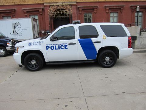 1991 Ford LTD Crown Victoria - white-and-blue Chevrolet SUV labeled 'Federal Protective Service Police' with a Homeland Security seal parked on pavement by brick building…