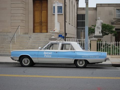 1991 Ford LTD Crown Victoria - light-blue and white vintage 'Detroit Police Tactical Mobile Unit' sedan parked curbside in front of a stone building with statue.