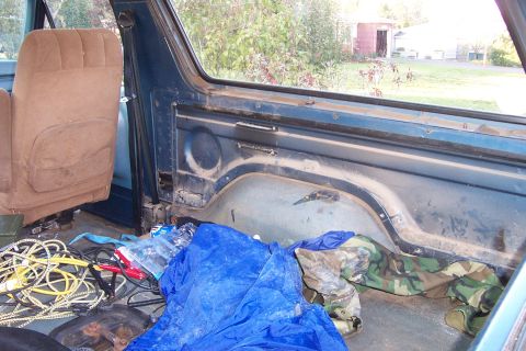 1980 Ford Bronco - The rear interior of a vehicle is cluttered with various items, including tarps and cables.