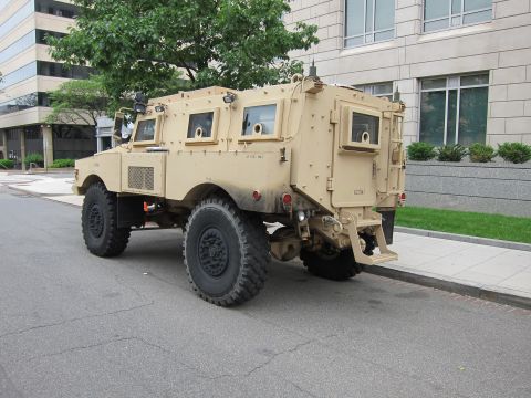 1991 Ford LTD Crown Victoria - Rear three-quarter view of a tan armored MRAP vehicle showing its boxy armored cab and rear bumper.