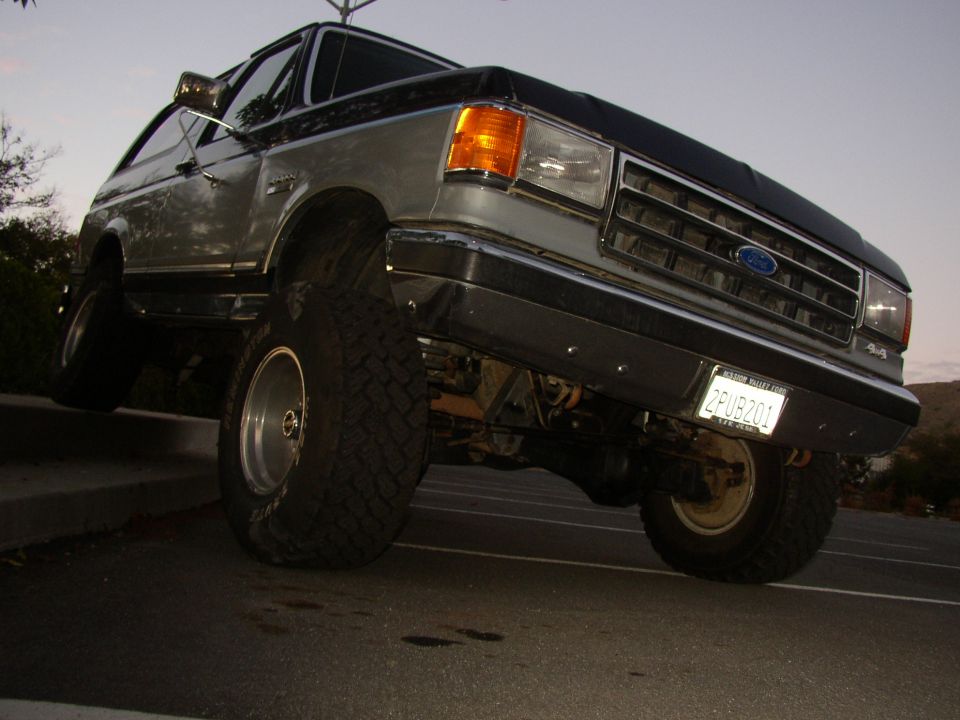 Low-angle view of lifted silver/black Ford SUV with big off-road tires at dusk