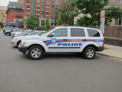 1991 Ford LTD Crown Victoria - Albany Police Dodge Durango with blue and orange markings parked among other vehicles on a street.