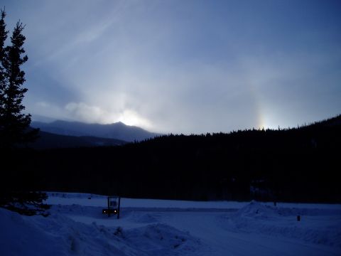 2009 Kenworth T800 - A winter scene unfolds with a small vehicle parked in the snow, set against a backdrop of mountains and a sky a sun dog.