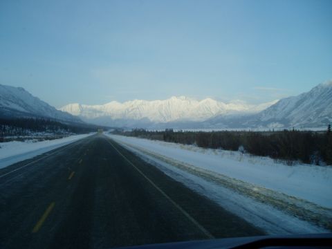 2009 Kenworth T800 - A desolate highway stretches towards snow-capped mountains under a clear blue sky.