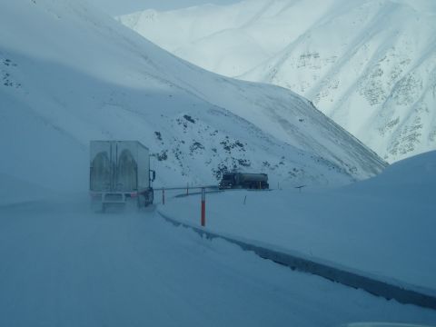 2009 Kenworth T800 - Two trucks navigate a treacherous snowy mountain pass, visibility reduced by blowing snow.