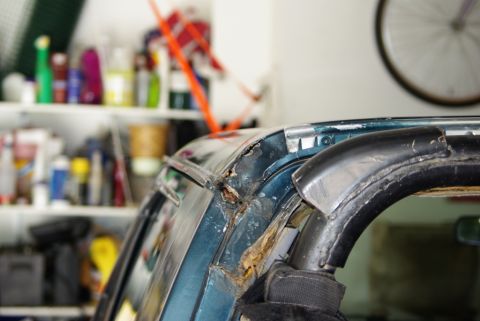 1995 Ford Bronco - Close-up view of a damaged roll bar and roofline on a teal SUV, with shelves of supplies in the background.