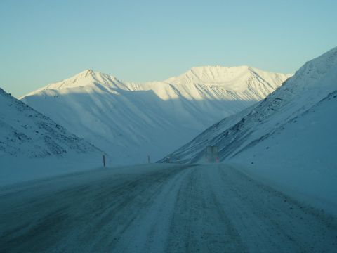 2009 Kenworth T800 - A truck navigates a snow-covered mountain pass, with snow-capped peaks visible in the distance.