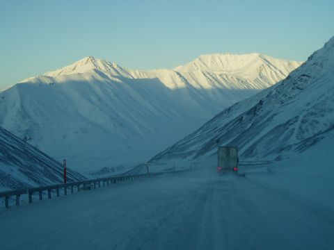 2009 Kenworth T800 - A truck travels down a snowy mountain pass under a clear blue sky.