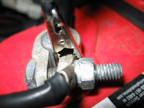 1992 Ford Bronco - Close-up view of a battery terminal connection with a jumper cable clip attached to the securing bolt.