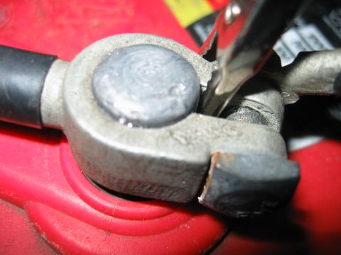 1992 Ford Bronco - A close-up view shows a car battery terminal clamp being connected to the battery post, with a jumper cable attached.