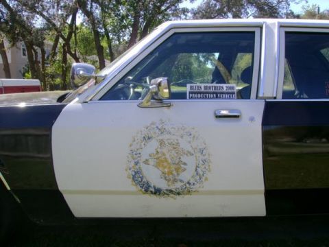 1991 Ford LTD Crown Victoria - Police car door with "Blues Brothers 2000 Production Vehicle" sticker and a faded emblem.