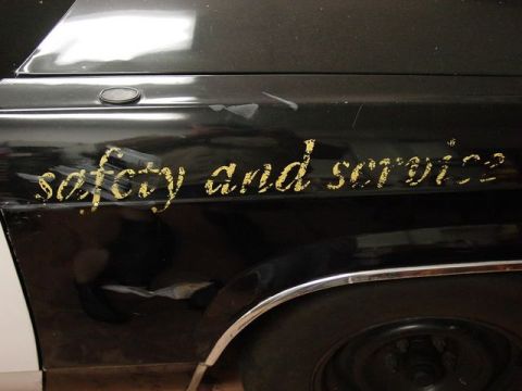 1991 Ford LTD Crown Victoria - A black car door displays gold lettering that reads "safety and service" above a chrome trim piece and tire.