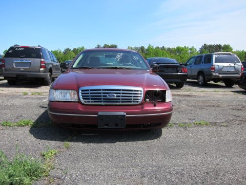 2001 Ford Crown Victoria - A maroon 2001 Ford Crown Victoria is parked in a lot, showing its front grille and missing headlight.