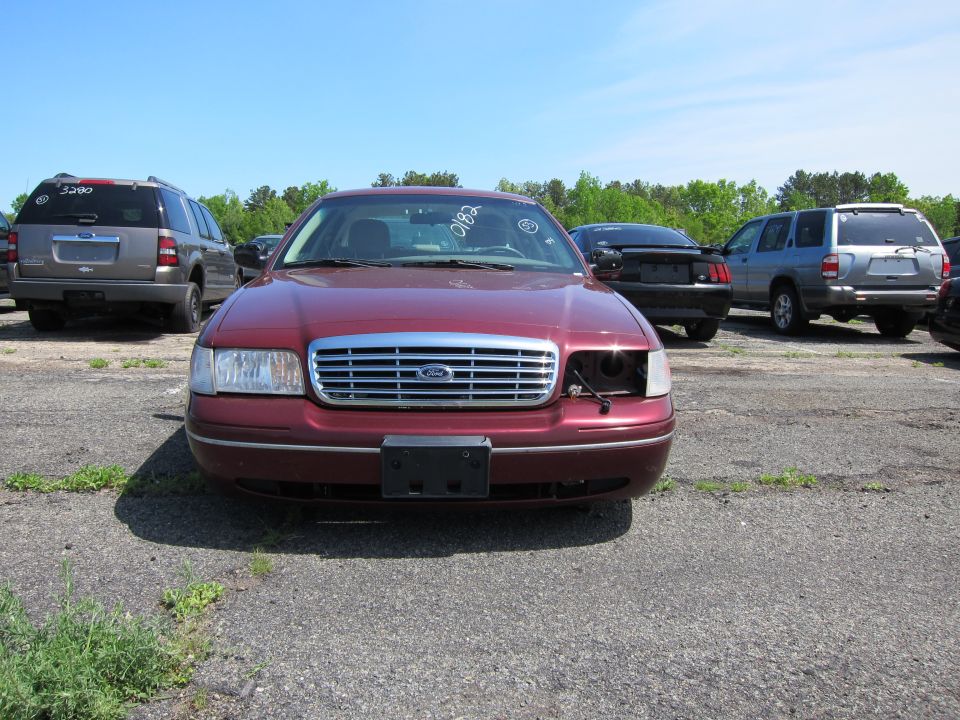 Front view of a maroon 2001 Ford Crown Victoria in a lot with other vehicles. The driver's side headlight is missing