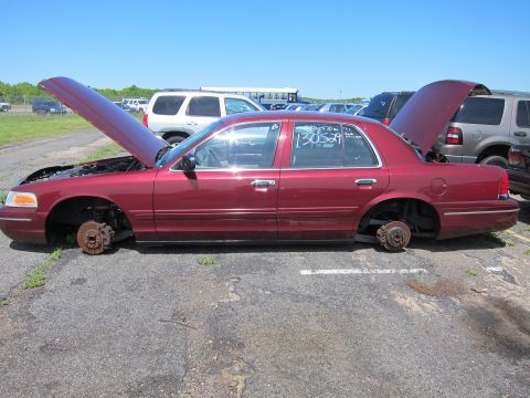 2001 Ford Crown Victoria - Maroon 2001 Ford Crown Victoria sits in a junkyard, missing its wheels and with hoods open.