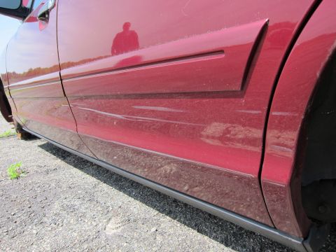 2001 Ford Crown Victoria - Close-up of a red car's side panel, revealing minor damage and a reflection of the photographer.