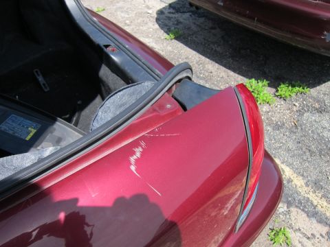2001 Ford Crown Victoria - Scratches mar the red paint on the trunk of a car, with another vehicle visible in the background.