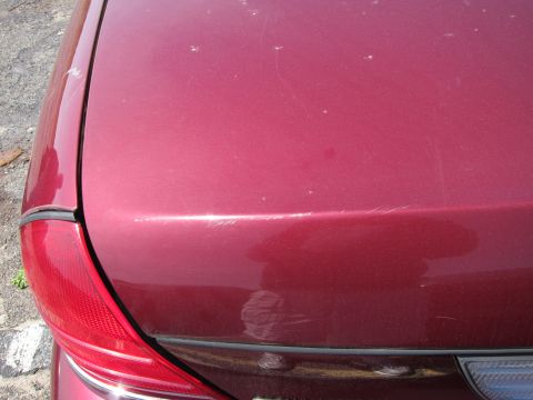 2001 Ford Crown Victoria - The rear of a red vehicle shows minor cosmetic damage on the trunk lid and around the taillight assembly.