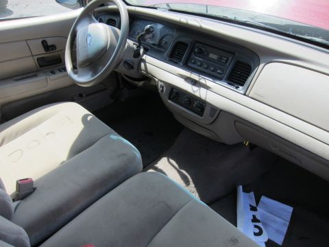 2001 Ford Crown Victoria - The interior of a 2001 Ford Crown Victoria features a tan dashboard, steering wheel, and seats, with some papers on the floor.