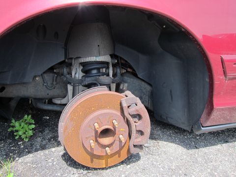 2001 Ford Crown Victoria - Front wheel well of a red 2001 Ford Crown Victoria, showing a rusty brake rotor and suspension components.