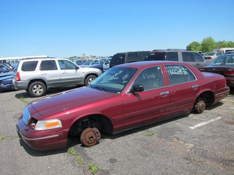 2001 Ford Crown Victoria - Junkyard Ford Crown Victoria, missing all four wheels, under a clear blue sky.