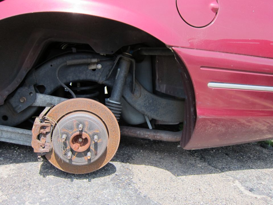 Rear wheel well of a red car showing rusty brake rotor, suspension components, and exhaust pipe