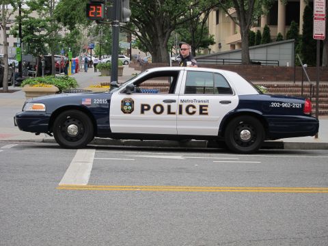 1991 Ford LTD Crown Victoria - black-and-white Metro Transit Police Ford Crown Victoria with an officer beside it at a street corner.