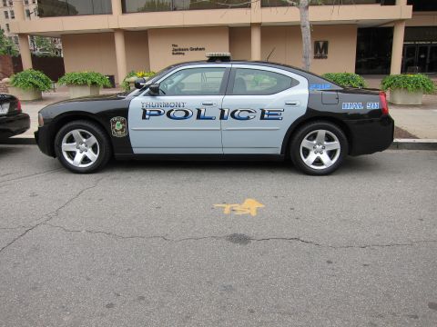 1991 Ford LTD Crown Victoria - black-and-silver Thurmont Police Dodge Charger with blue lettering parked on a street by an office building.
