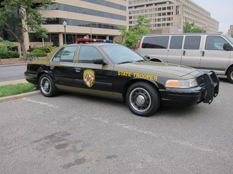 1991 Ford LTD Crown Victoria - black-and-tan Maryland State Trooper Ford Crown Victoria police sedan parked along a city curb near tall office buildings.