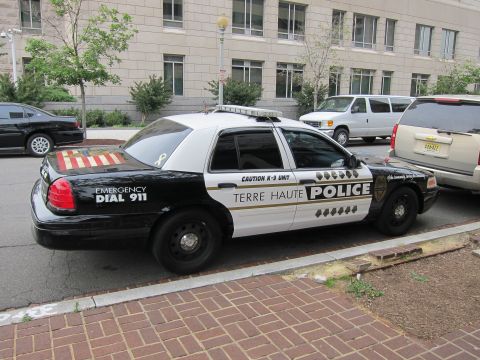 1991 Ford LTD Crown Victoria - black-and-white Terre Haute Police Ford Crown Victoria K-9 cruiser parked at a curb beside a brick sidewalk.