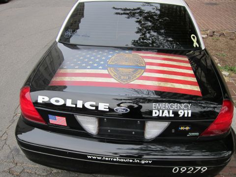 1991 Ford LTD Crown Victoria - Rear of a black Terre Haute Police Ford cruiser with an American flag trunk wrap and POLICE / DIAL 911 lettering.