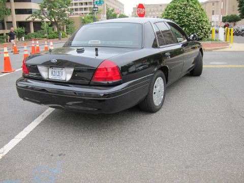 1991 Ford LTD Crown Victoria - Rear-quarter view of an unmarked black Ford Crown Victoria sedan parked on a street near a stop sign and traffic cones.
